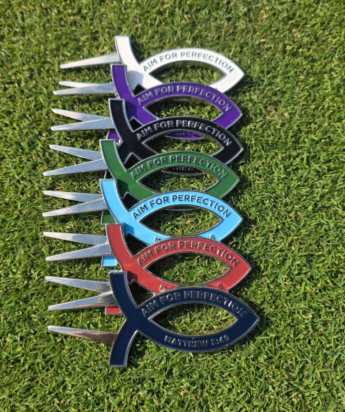 All seven Aim for Perfection divot tool colors fanned out on a golf green